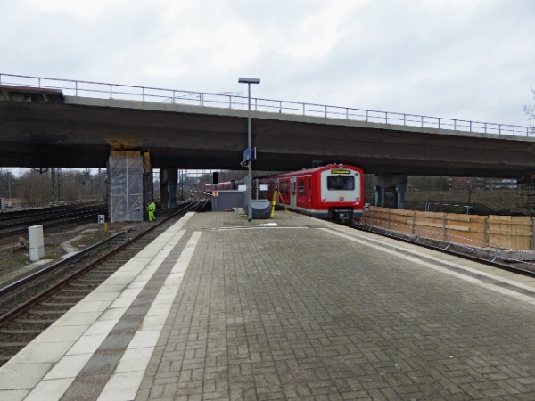 Eine S-Bahn verlässt den Stellinger Bahnhof in Richtung Eidelstedt/Pinneberg durch die Baustelle unter der Langenfelder Brücke hindurch. Der Bahnsteig selbst reicht fast bis unter die Brücke.