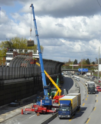 Die alte Lärmschutzmauer am Nienredder wird von der Autobahnseite her abgebrochen. Der Kran hebt von der Autobahn her Teile heraus.