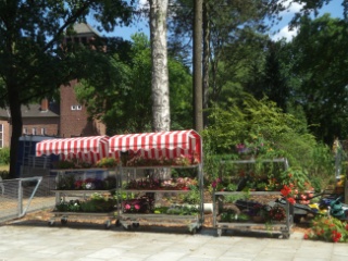Tische und Borte mit Sonnenschutz für Pflanzen auf der Freifläche vor dem neuen Blumenladen.