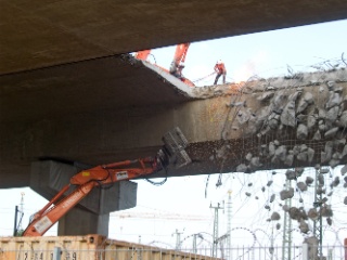 Aus der Brücke hängende Stahlseile werden per Hand mit dem Schweißbrenner getrennt.