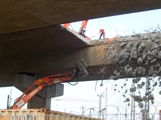 Seitlich aus der Brücke hängende Stahlseile werden per Hand mit einem Schweißbrenner durchtrennt.